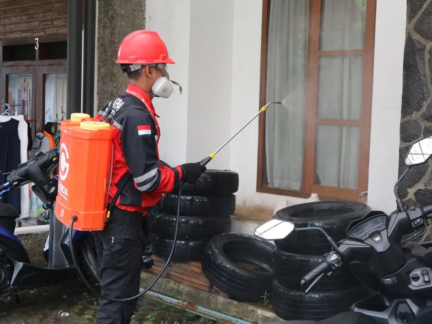 A licensed pest control technician applying an exterior barrier spray around a window frame, the standard fall treatment for box elder bugs
